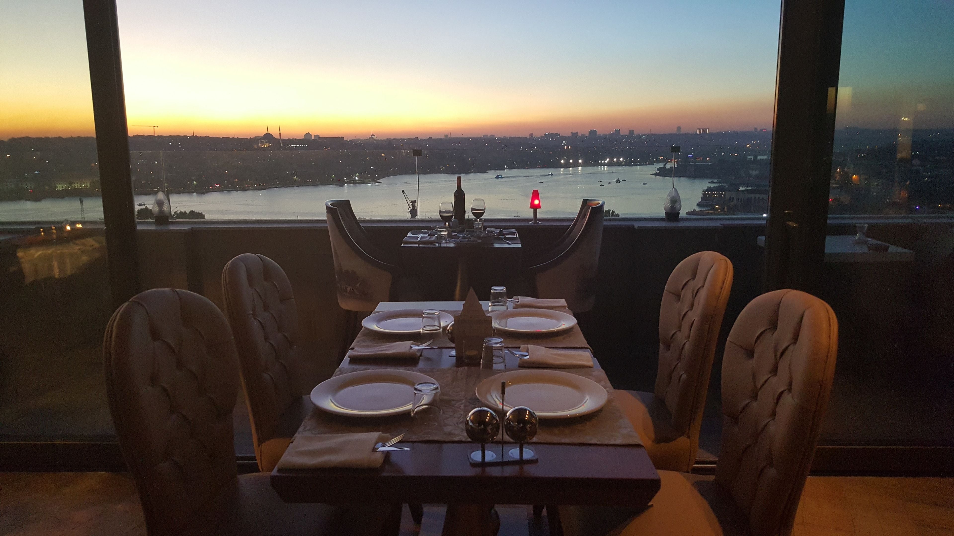 A dining table set for four with a view of a cityscape and river at dusk.
