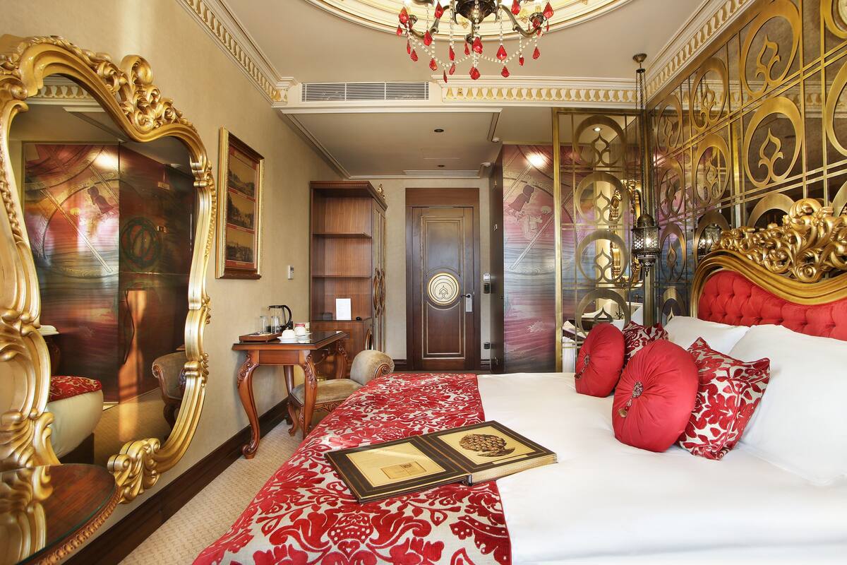 A luxurious bedroom with a large ornate mirror, a plush red and white patterned bedspread, and a classic wooden nightstand.