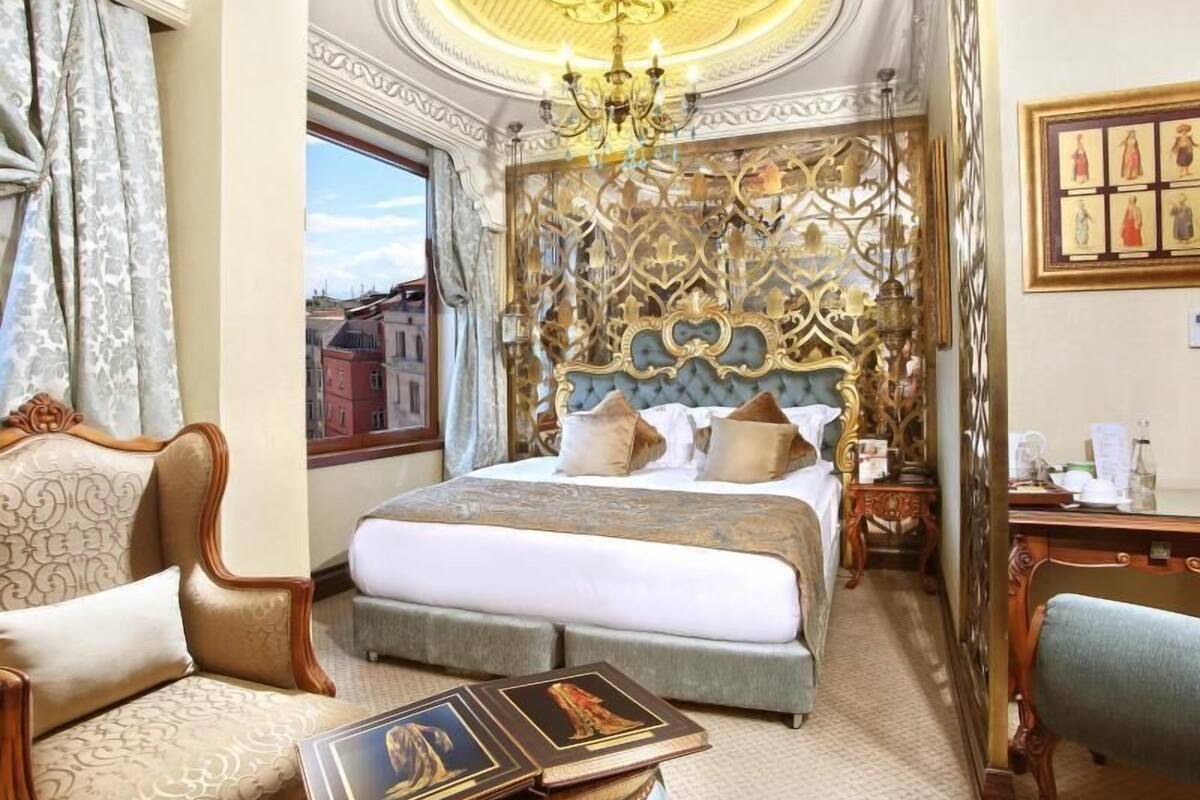 A luxurious hotel room with a large bed, ornate headboard, and a chandelier.
