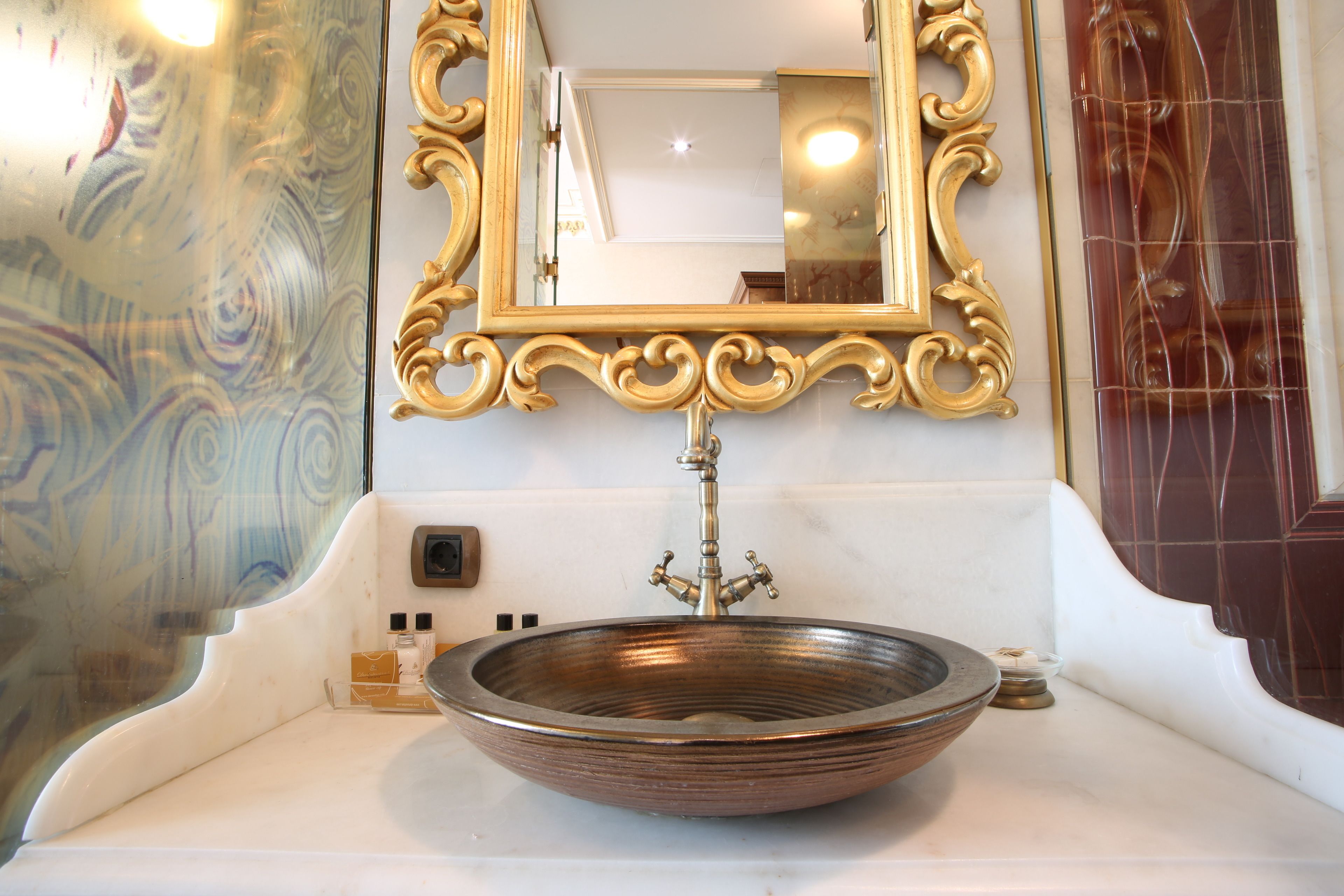 A bathroom with a large, ornate mirror, a vessel sink, and a decorative wall.