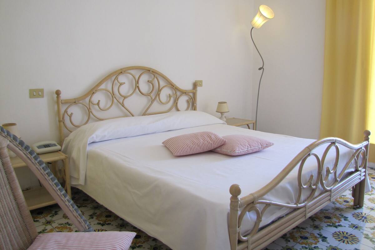 Un lit avec un matelas blanc et un cadre en métal, une table de chevet avec une lampe et un luminaire fixé au mur.