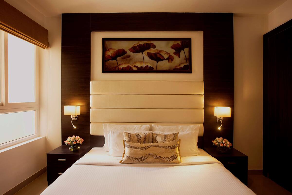A hotel room with a large bed, two bedside tables with lamps, a wall-mounted painting, and a window.