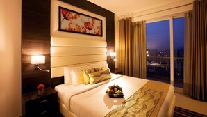 A hotel room with a large bed, a nightstand with a lamp, a decorative wall piece, and a view of the city at night.