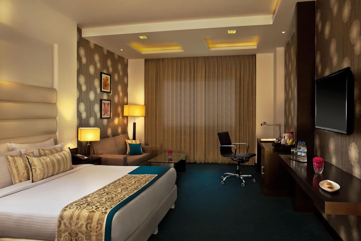 A hotel room with a large bed, a desk, a chair, a TV, and a window with curtains.