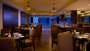 A restaurant with multiple dining tables and chairs, overhead lighting, and a view of the street outside.