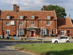 A traditional brick building with a red-tiled roof, a prominent sign for 'The King's Head Hotel', and outdoor seating with potted plants. - The Kings Head Hotel (Dereham)