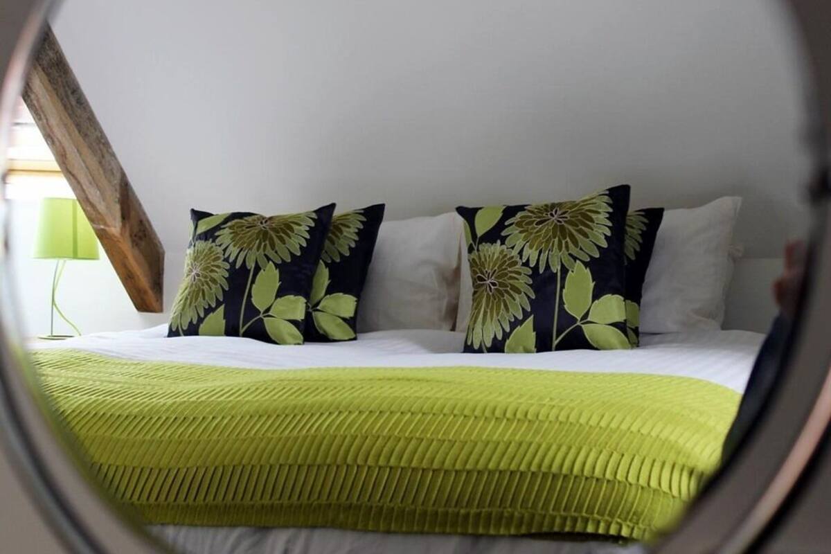 A bed with a green textured blanket, two pillows with a leaf pattern, and a white wall.
