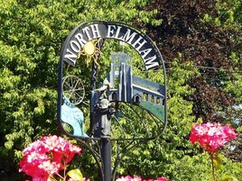 Un cartel con el texto 'NORTH ELMHAM' y una bicicleta.