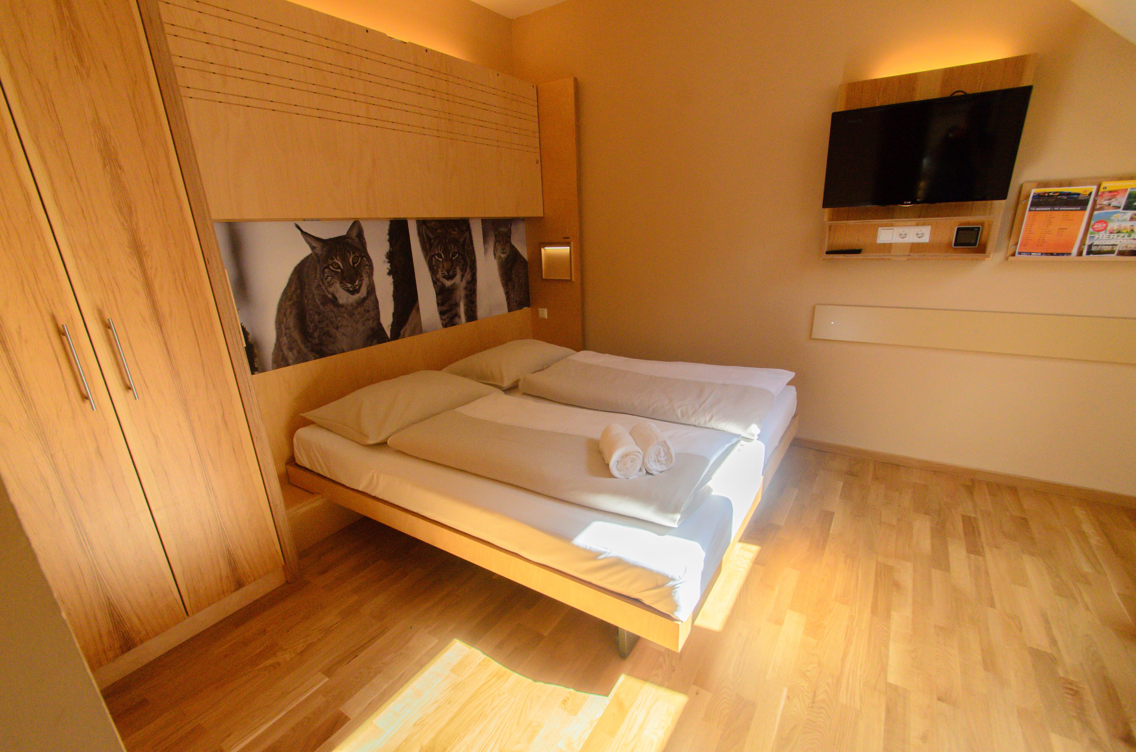 Habitación con cama, armario de madera y televisor montado.