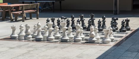 A chessboard set up outdoors with tables and chairs in the background.