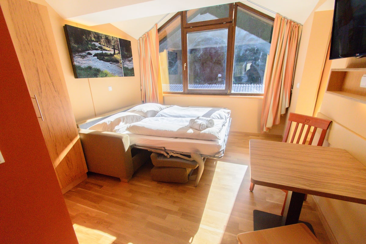 A compact hotel room with a bed, a dining table, and a TV.