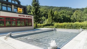 Un hôtel avec une piscine à eau claire, un panneau indiquant « JUFA », et un paysage montagneux en arrière-plan.