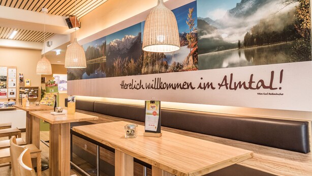 L’intérieur d’un restaurant est agrémenté de tables en bois, de luminaires suspendus et d’une fresque murale représentant un paysage montagneux.