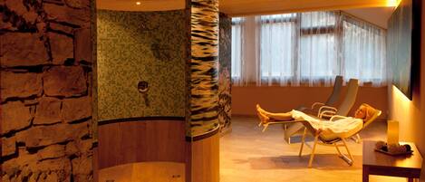 Un cuarto de spa con pared de piedra, pared de mosaicos y techo de madera. Hay dos sillones reclinables y una mesita con una bandeja de objetos.