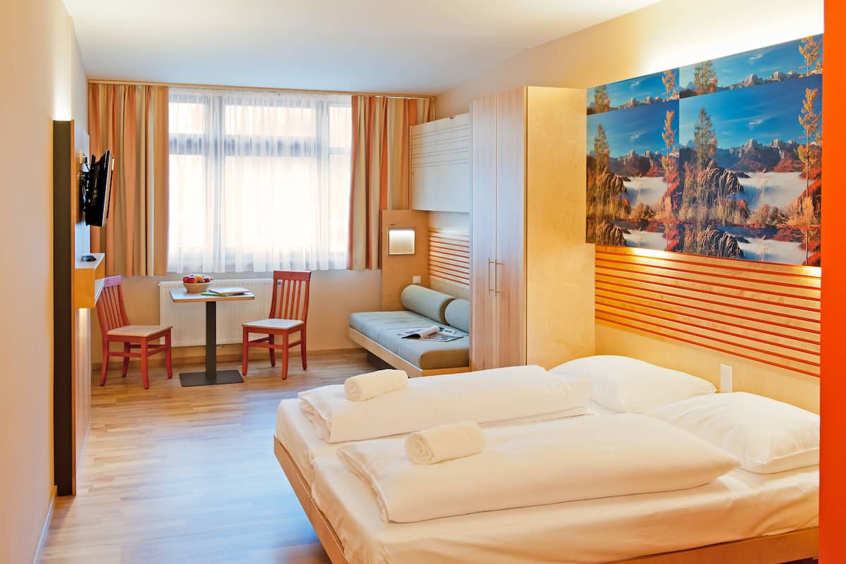 Habitación de hotel con una cama, un escritorio con sillas, un sofá y un cuadro en la pared.