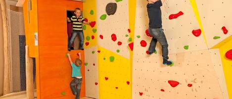 A climbing wall with colorful holds, a small play area with a toy car, and a netted play structure.