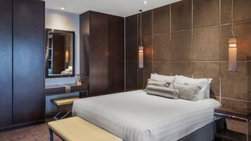A modern hotel room with a large bed, a bench, a vanity with a mirror, and two wall-mounted lights.