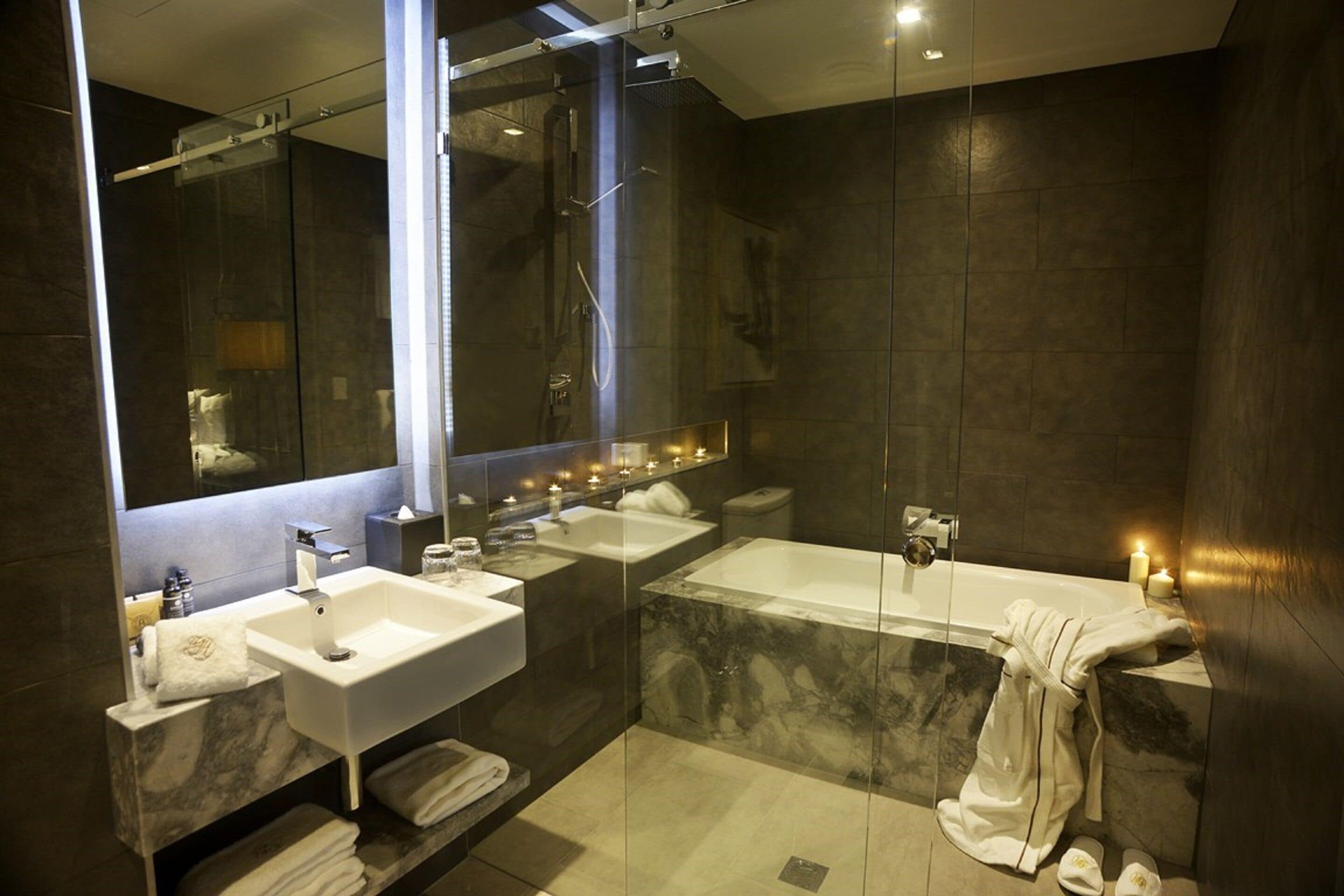 A modern bathroom with a glass-enclosed shower, two sinks, a bathtub, and a large mirror.