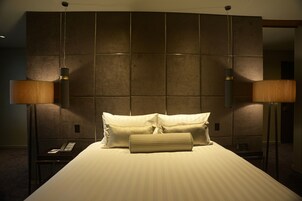 A hotel room with a large bed, two bedside lamps, and a modern headboard.