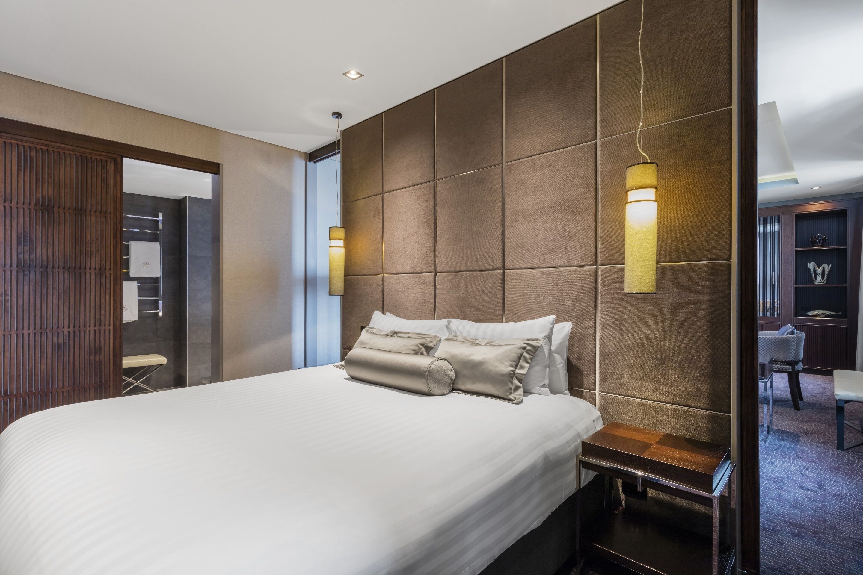 A modern hotel room with a large bed, a wooden headboard, and a small bedside table.