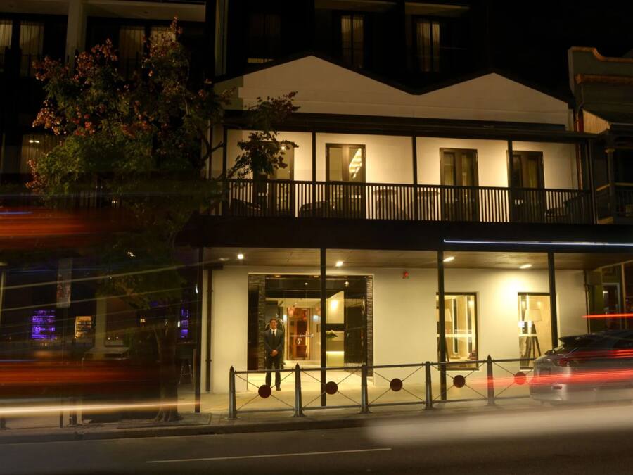 A hotel with a modern design, featuring a balcony and a well-lit entrance.
