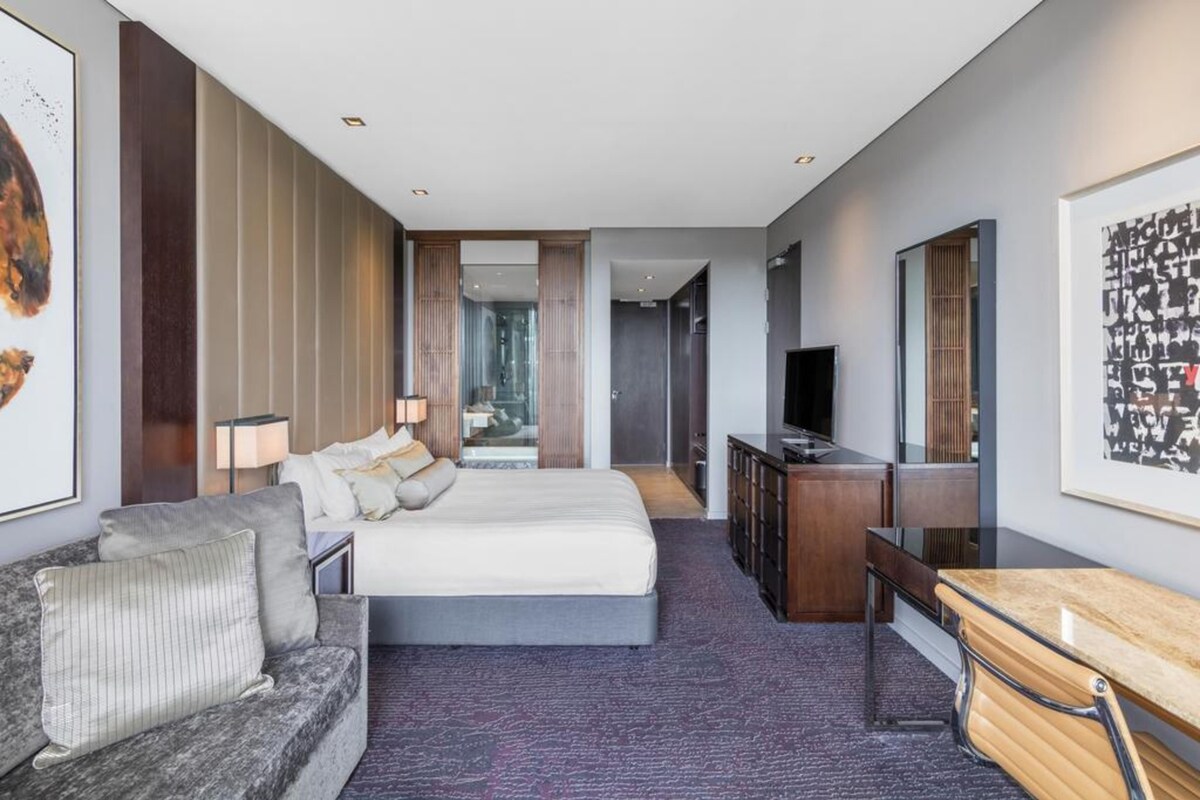Una habitación de hotel moderna con una cama, un escritorio, un televisor y una obra de arte grande en la pared.