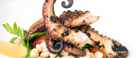 A plate of grilled octopus with vegetables and herbs.