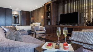 A modern hotel room with a large bed, a sofa, a dining table with a tray of desserts and glasses of wine, and a flat-screen TV mounted on the wall. - The Beetson Hotel (Petrie Terrace)