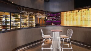 A bar area with a round table and two white wire chairs, shelves of bottles, and a TV mounted on the wall. - The Beetson Hotel (Petrie Terrace)