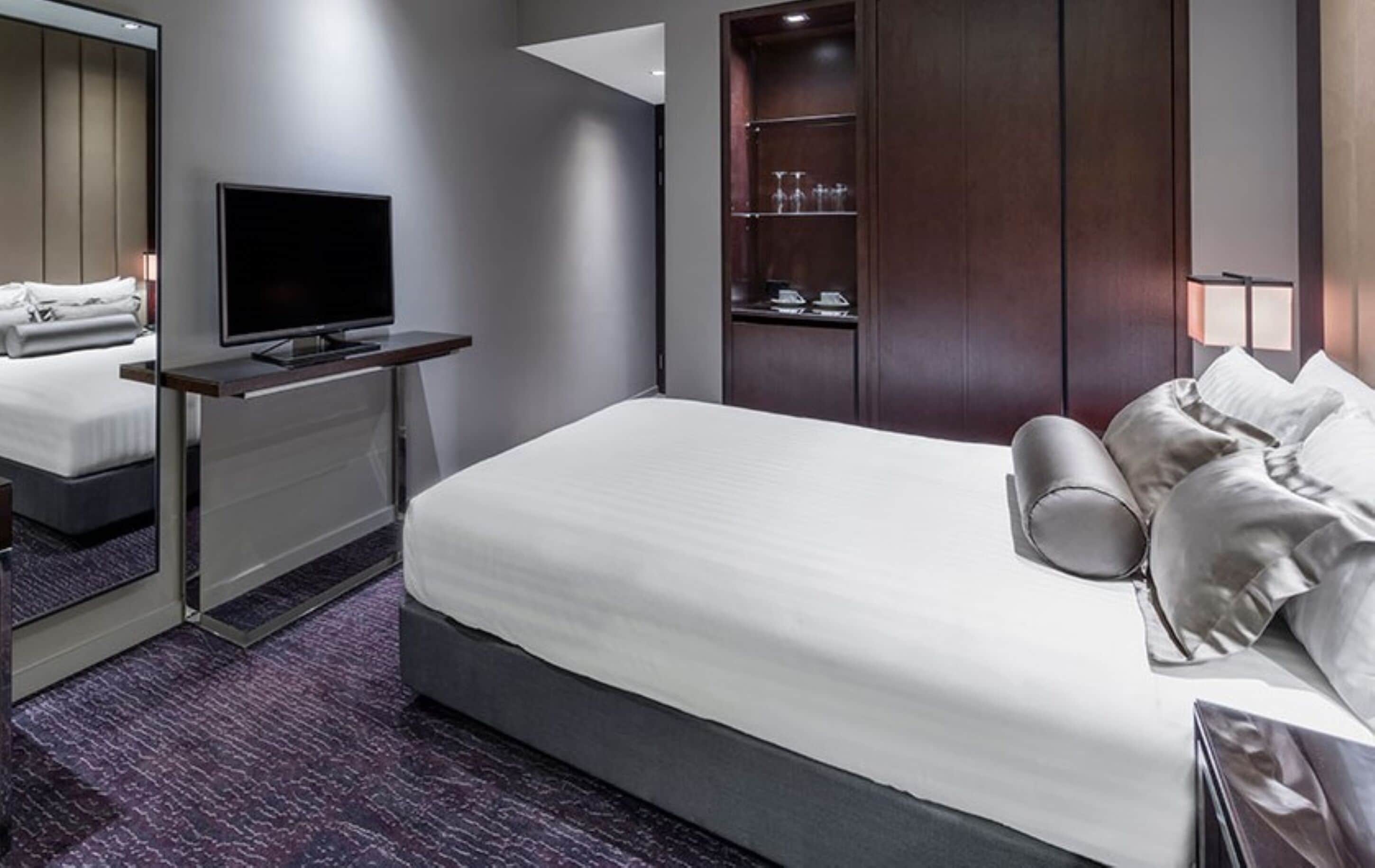 Habitación de hotel con una cama grande, un televisor de pantalla plana, un armario de madera y un pequeño rincón de descanso.