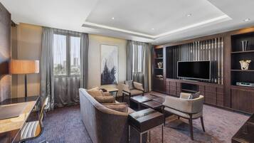 Una habitación de hotel moderna con sofá, sillones, una mesa de centro, televisor y estantería.
