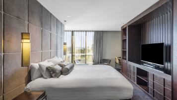 Una habitación de hotel moderna con una cama grande, televisión de pantalla plana, zona de estar y un amplio ventanal con cortinas.