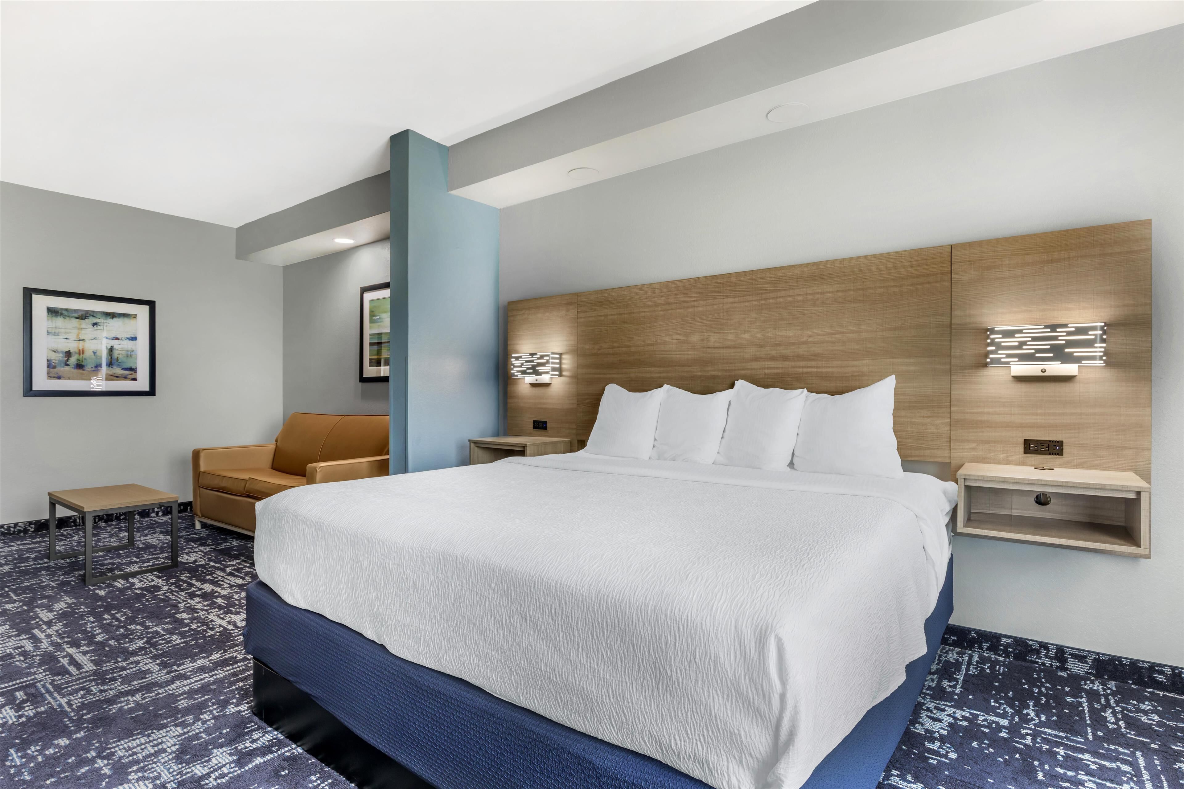 Ein modernes Hotelzimmer mit einem großen Bett, einer Couch, einem kleinen Tisch und Wandleuchten.