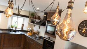 A modern kitchen with wooden cabinets, a central island, and hanging light bulbs. - The Royal Oak Exmoor (Minehead)
