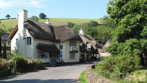 A traditional white building with a thatched roof, likely a pub or inn, with a signboard and a small garden area. - The Royal Oak Exmoor (Minehead)