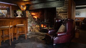 A cozy bar area with a stone fireplace, leather armchair, and wooden bar stools. - The Royal Oak Exmoor (Minehead)