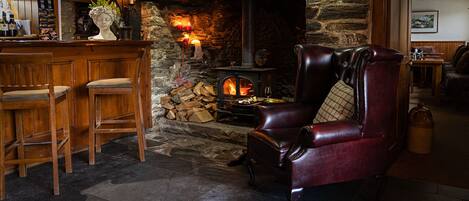A cozy bar area with a stone fireplace, leather armchair, and wooden bar stools.