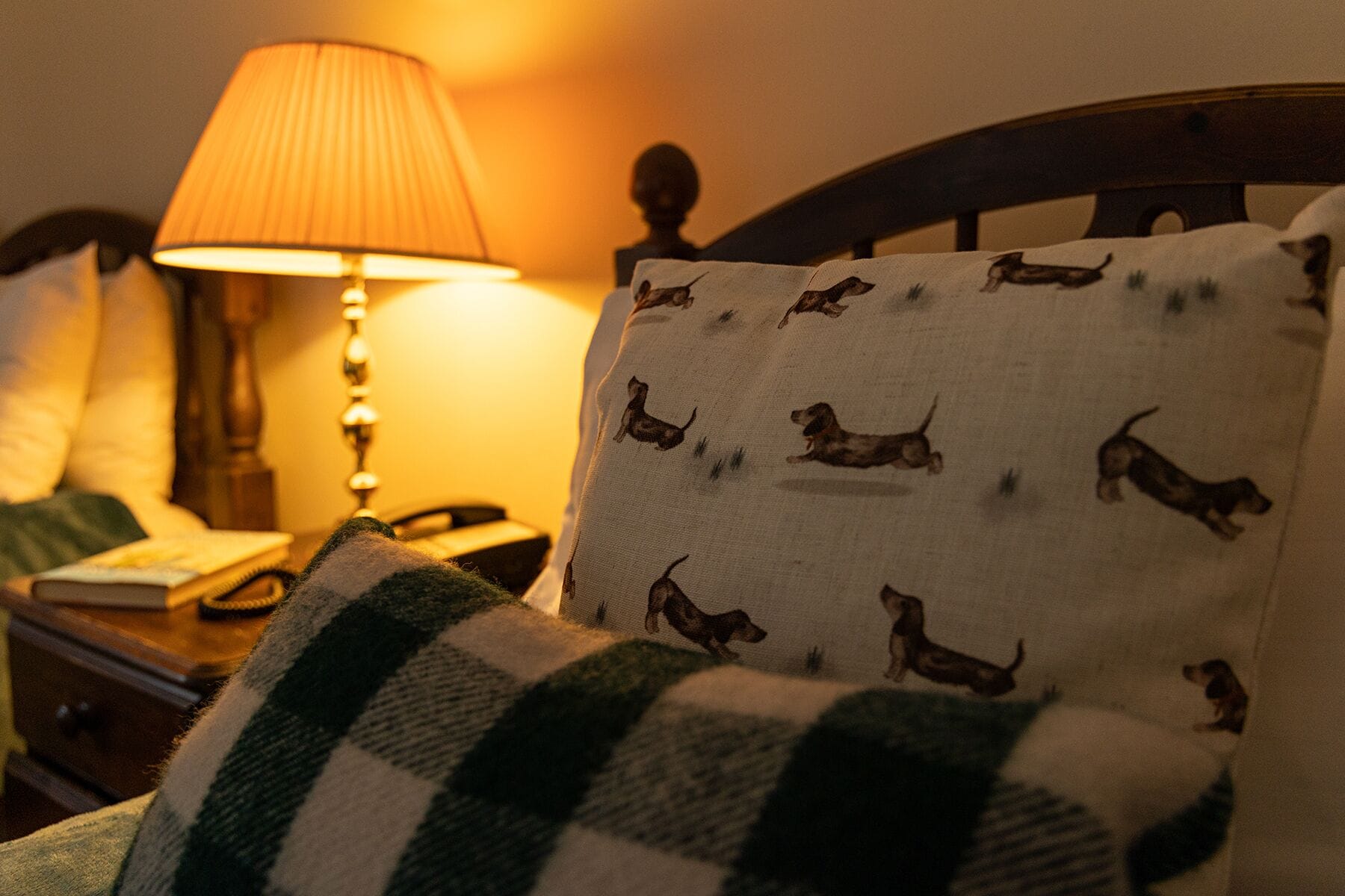 A bed with a pillow featuring a dog pattern, a lamp, and a book on a bedside table.