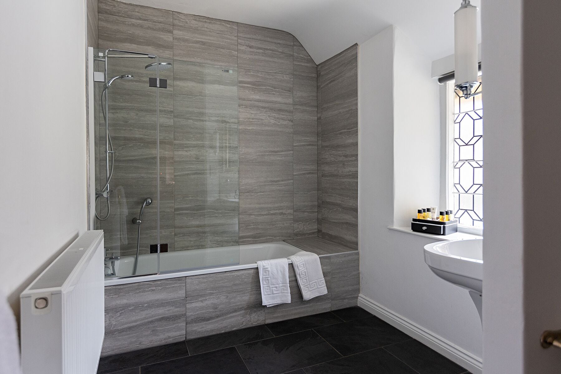 A modern bathroom with a glass-enclosed shower, a freestanding bathtub, and a white sink with a geometric window design.