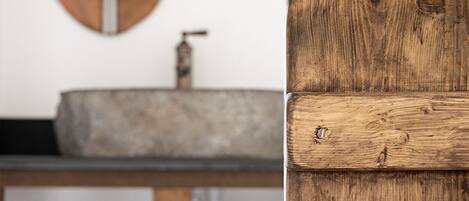 A rustic bathroom with a wooden vanity, a round mirror, and wicker baskets on shelves.