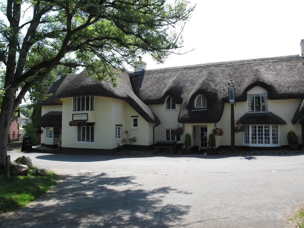 Een traditioneel gebouw met rieten dak en een bord waarop staat: 'The Red Cow Inn'.