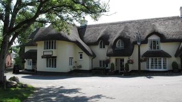 Een traditioneel gebouw met rieten dak en een bord waarop staat: 'The Red Cow Inn'.