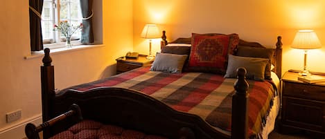 A neatly made bed with a checkered blanket, two bedside lamps, a nightstand with a phone, and a window with curtains.