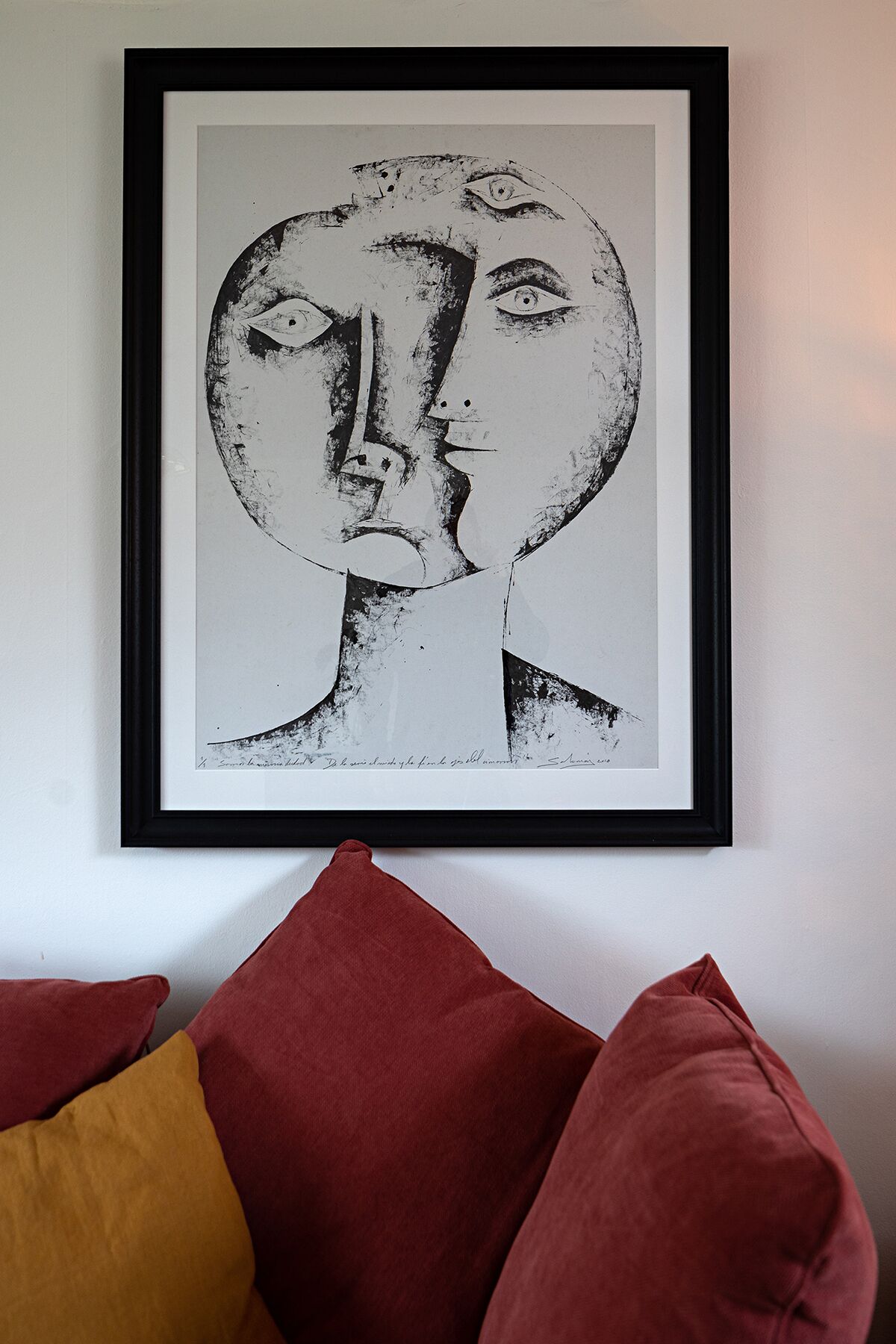 Una obra de arte en un marco colgada en una pared, con un sofá rojo al frente.