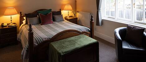 A bedroom with a bed, bedside lamps, a radiator, a chair, and a window with curtains.