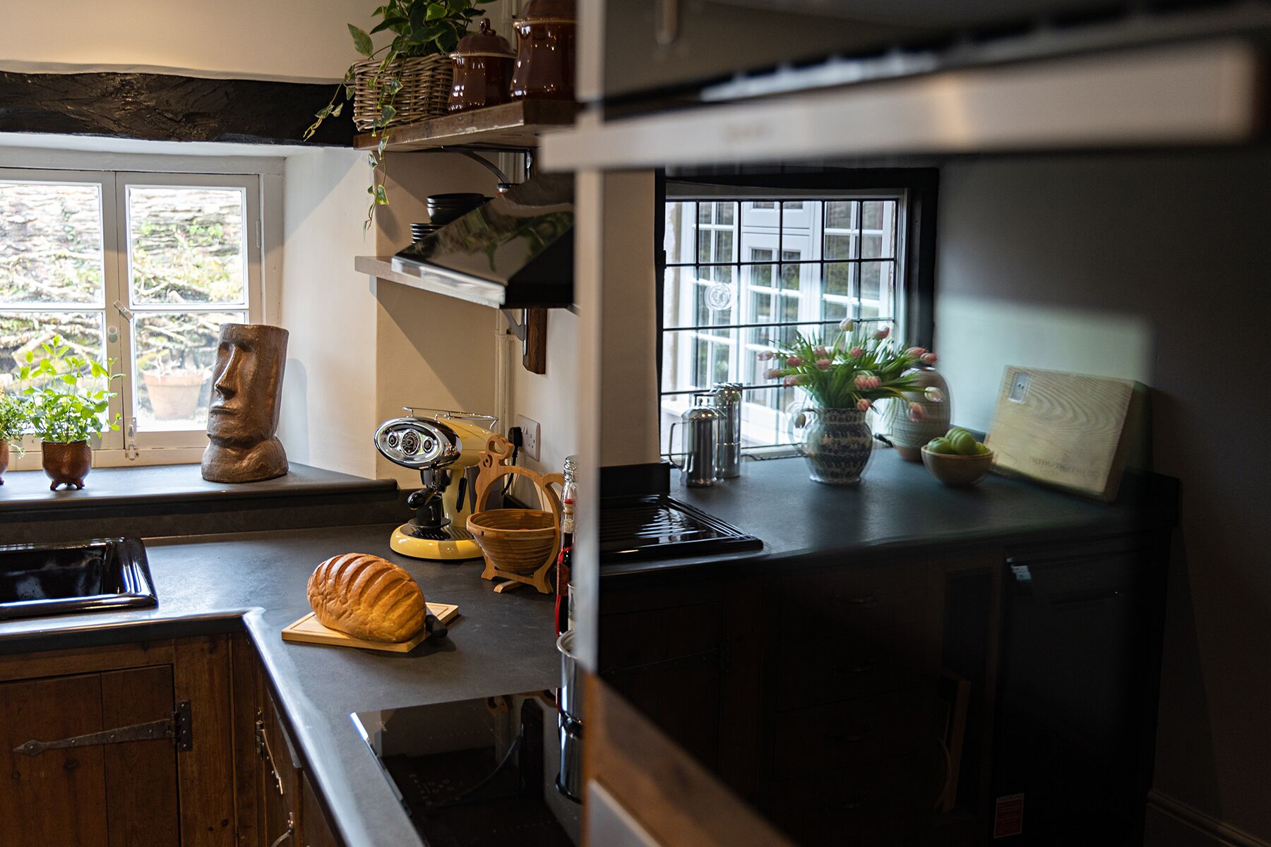 Una cocina con encimera de madera, hogaza de pan, cafetera y diversos utensilios de cocina.