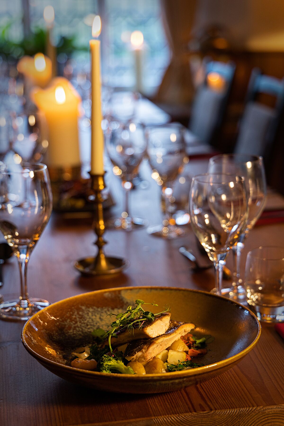 A dining table with a candle, wine glasses, and a bowl of food.