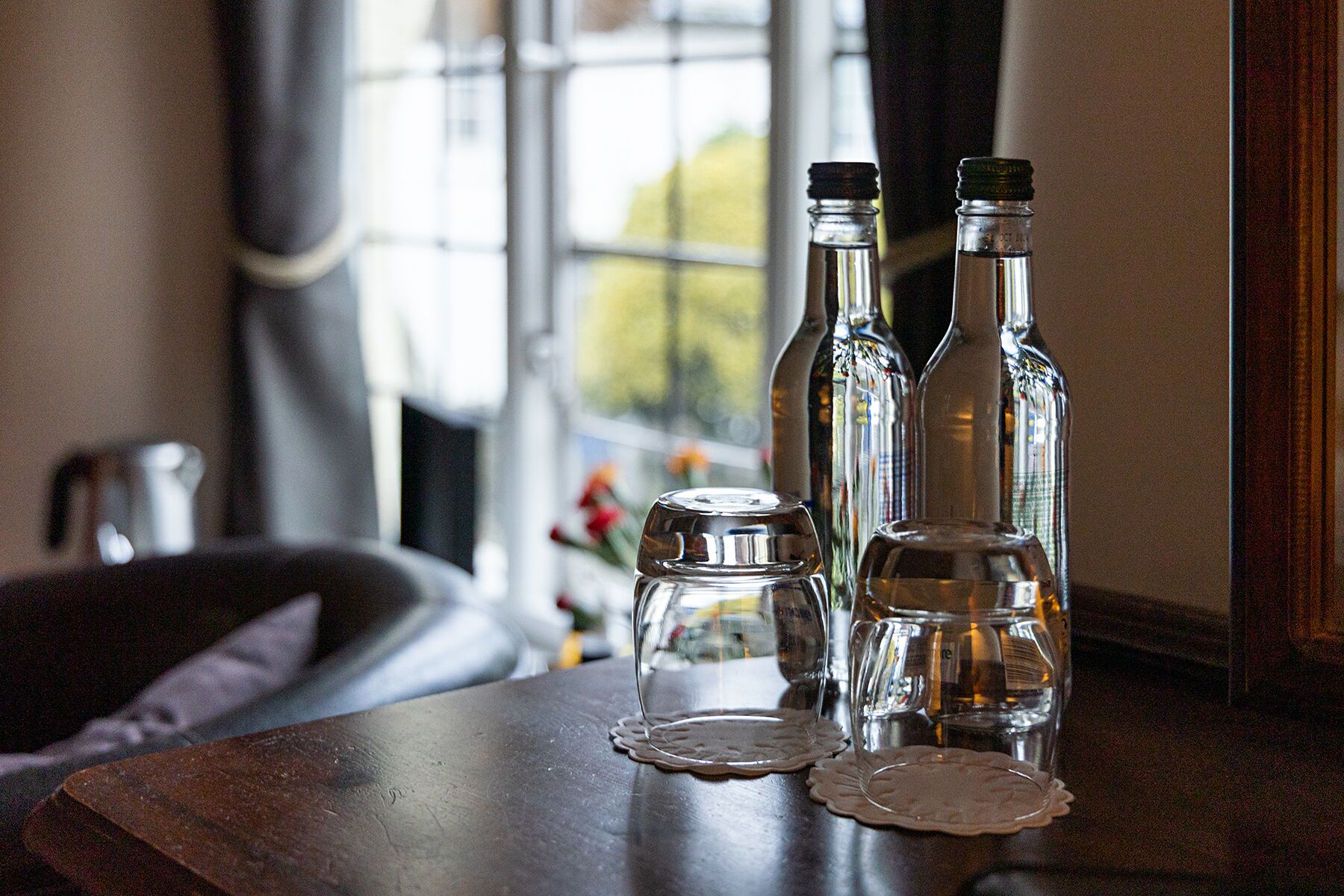 Ett träbord med tre glasflaskor och ett glas placerat på en spetsduk.
