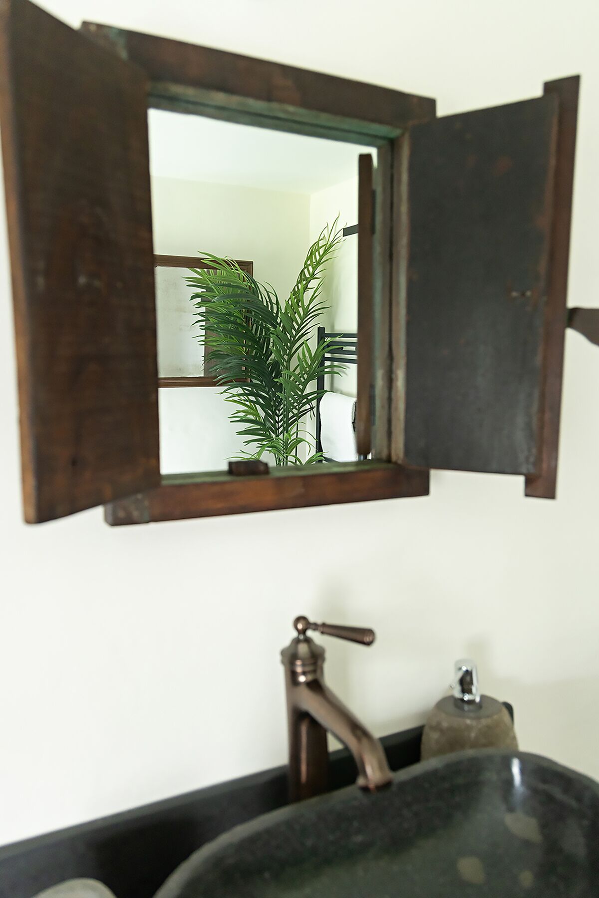 Un baño con un espejo de marco de madera, un lavabo negro y una planta verde.