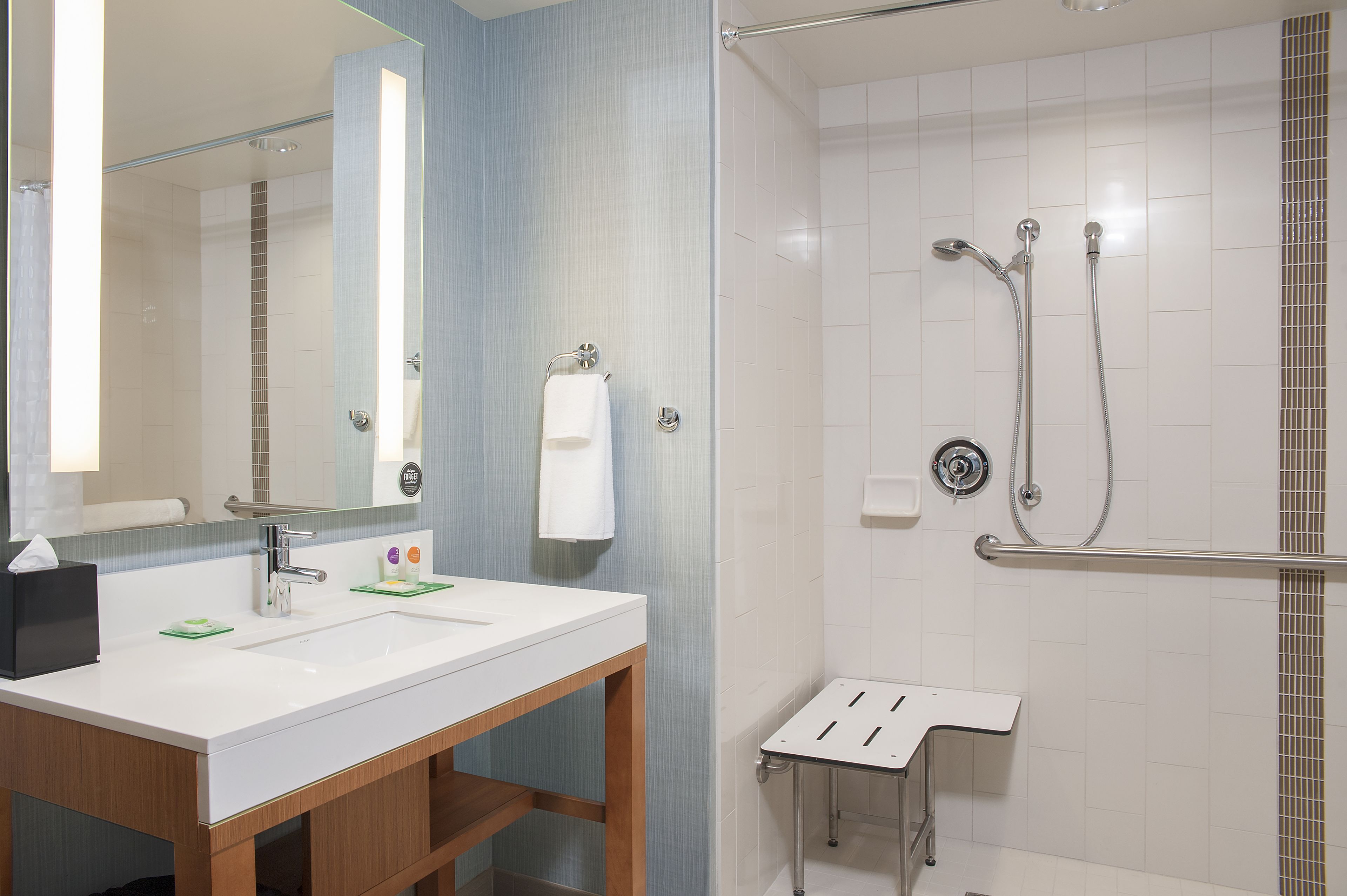 Un baño moderno con lavamanos doble, un espejo, toallero y zona de ducha con barra de apoyo.